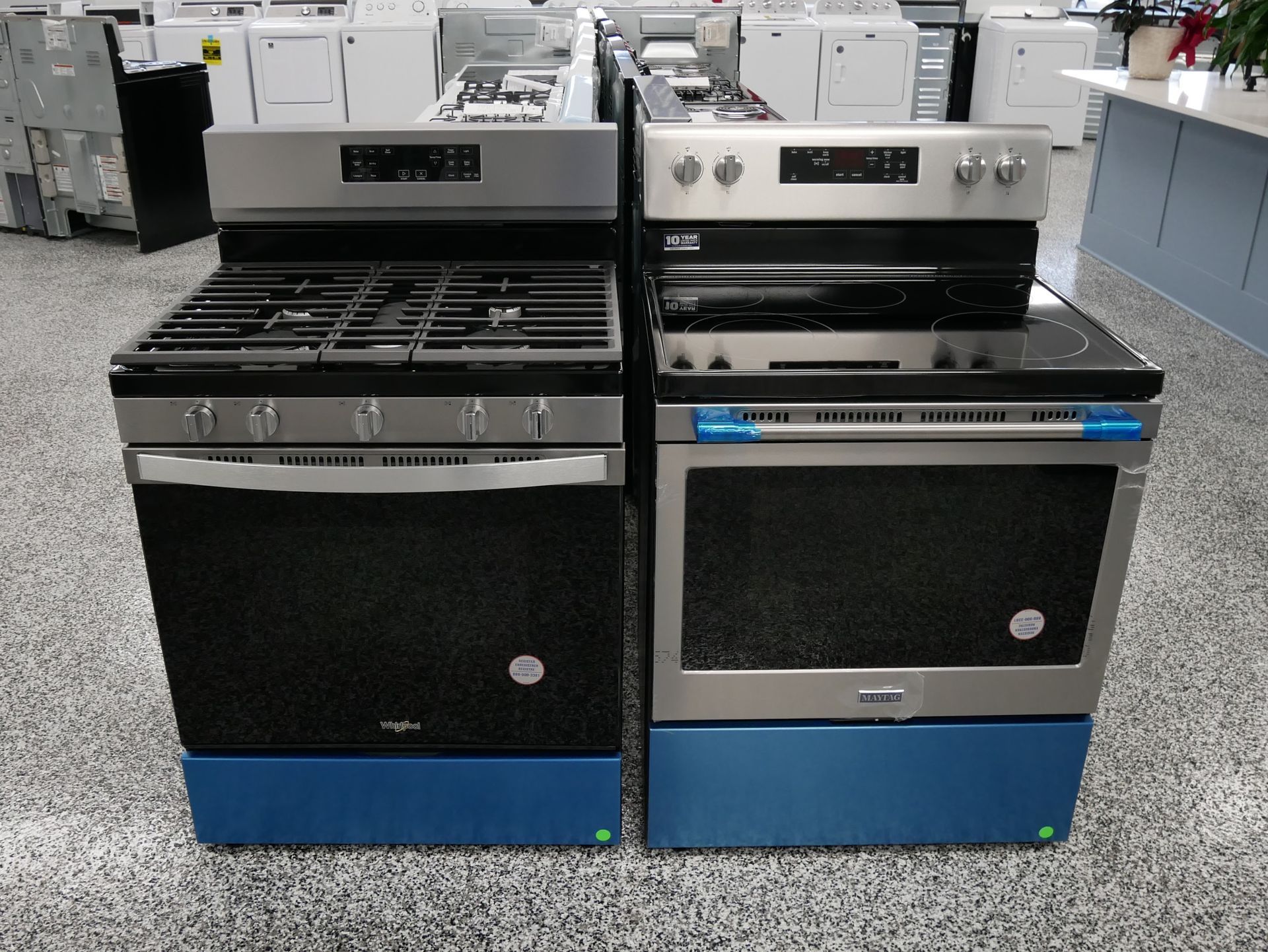 Two stoves: gas and electric, stainless steel finish, on a showroom floor.