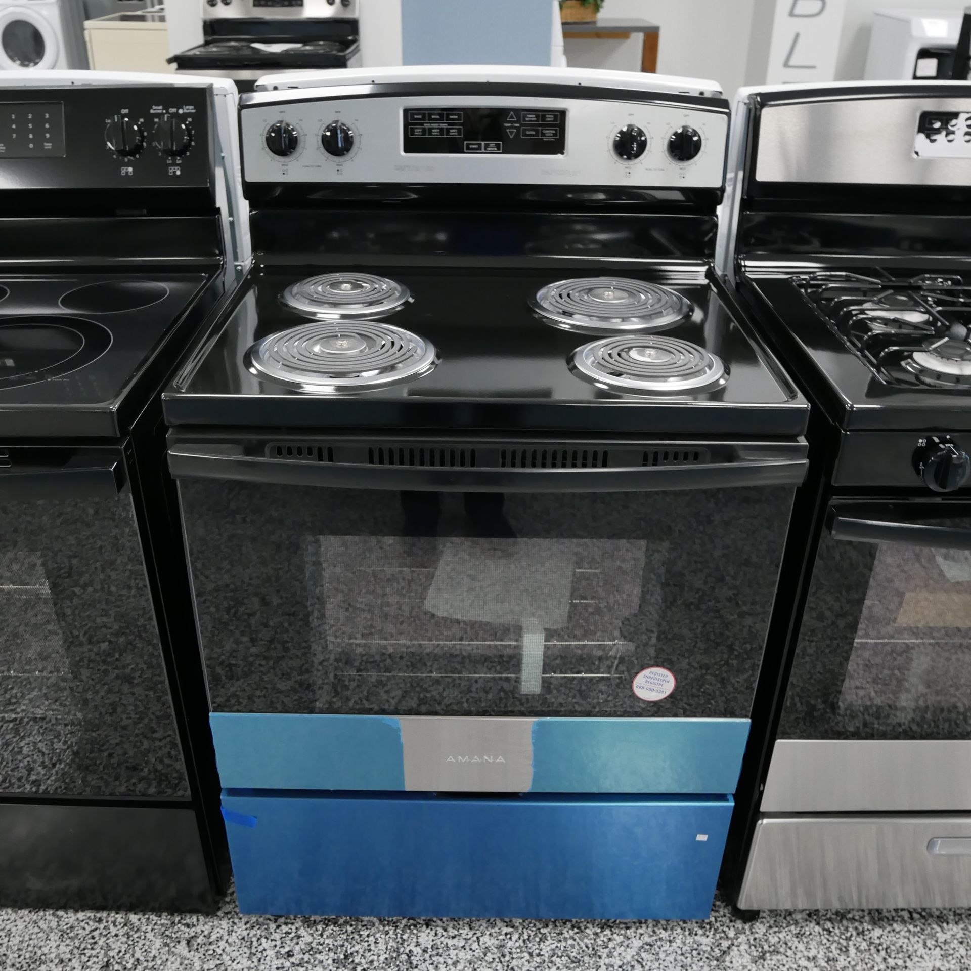 Electric range with black cooktop and oven, stainless steel trim, four burners, in a showroom.