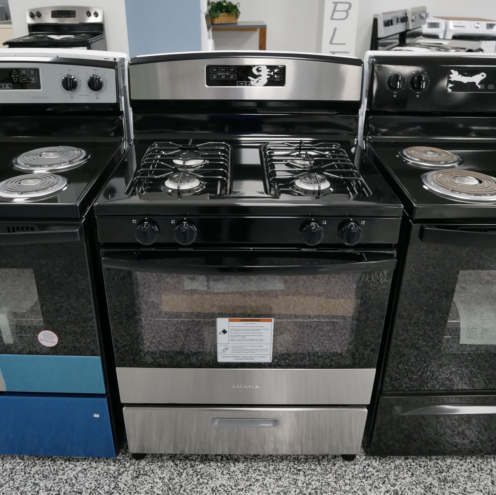 Three kitchen ranges: a stainless steel gas range flanked by black electric ranges.