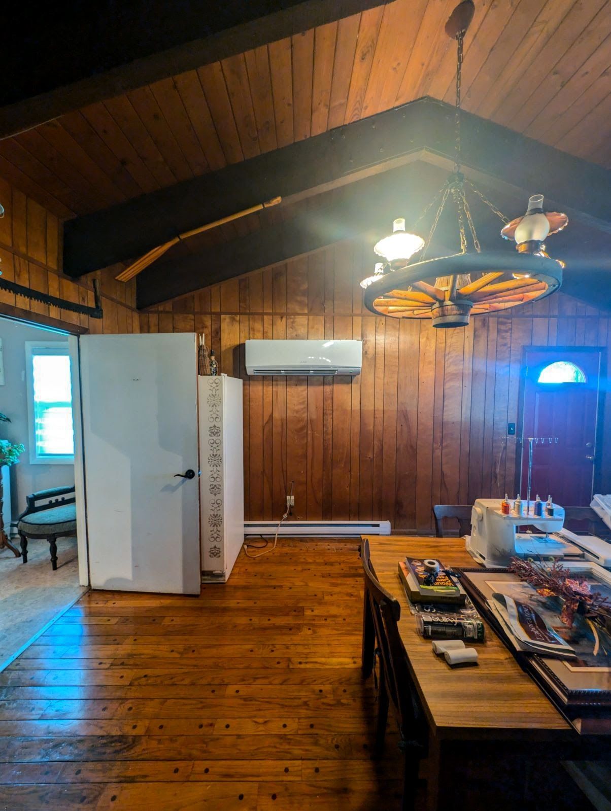 Wooden-paneled room with brown floors and ceiling, a chandelier, air conditioner, and a table with items.