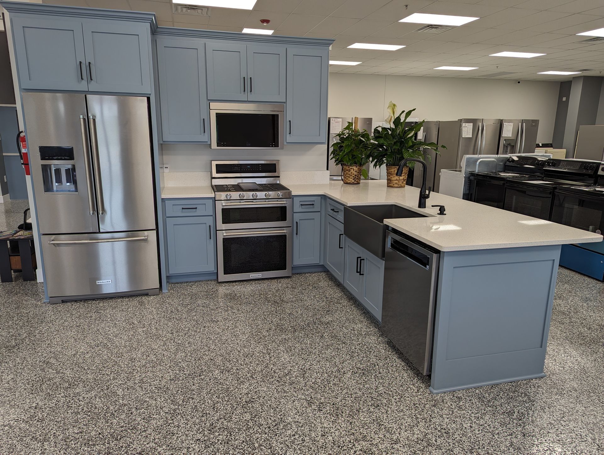 Blue kitchen display with stainless steel appliances, white countertops, and an island.