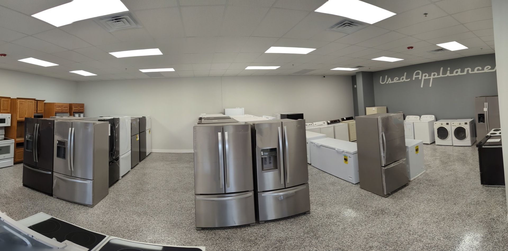 A showroom with numerous refrigerators on display. The room is well-lit, and the floor is speckled.