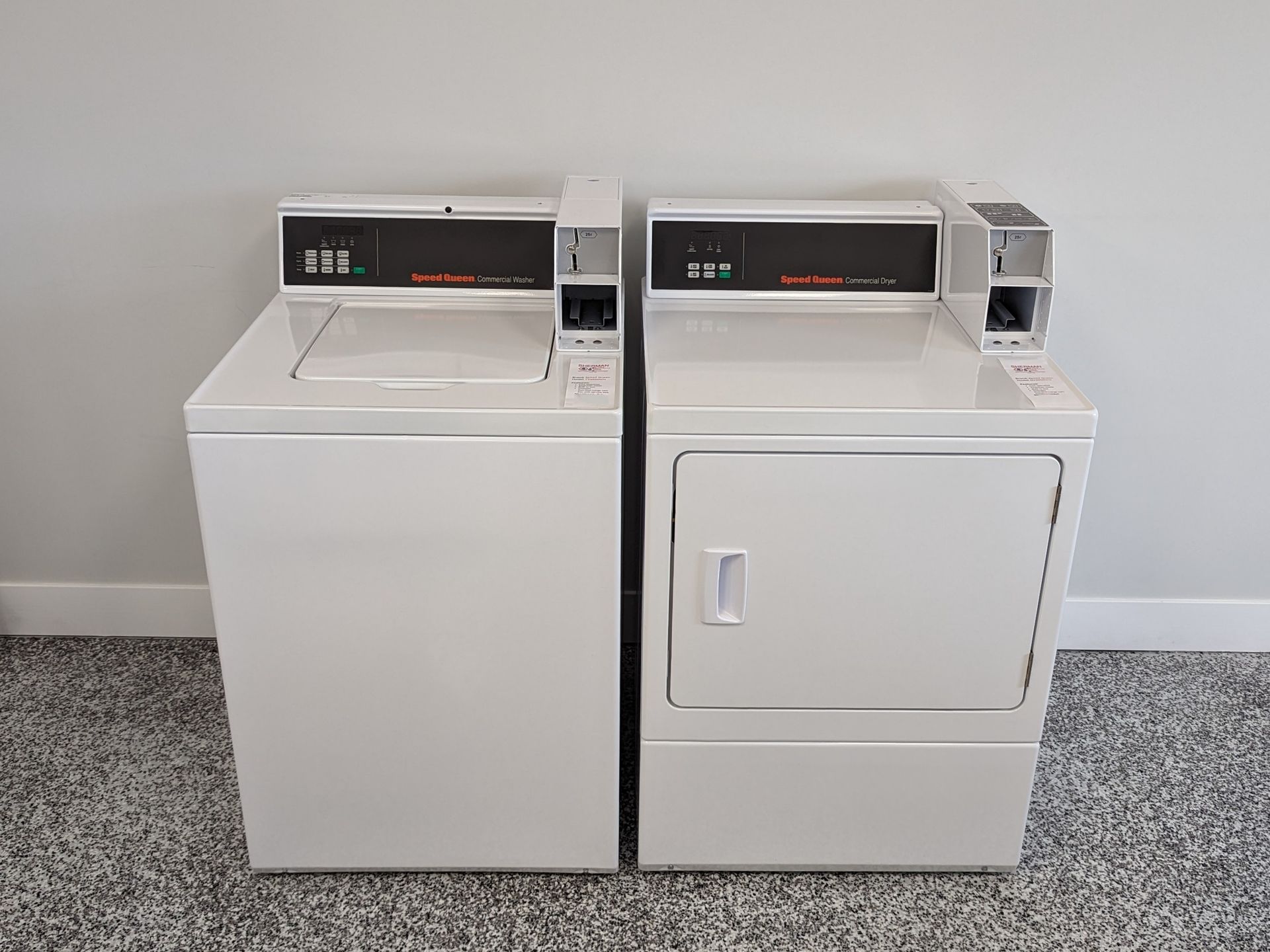 White commercial washer and dryer in a laundry room, coin operated.