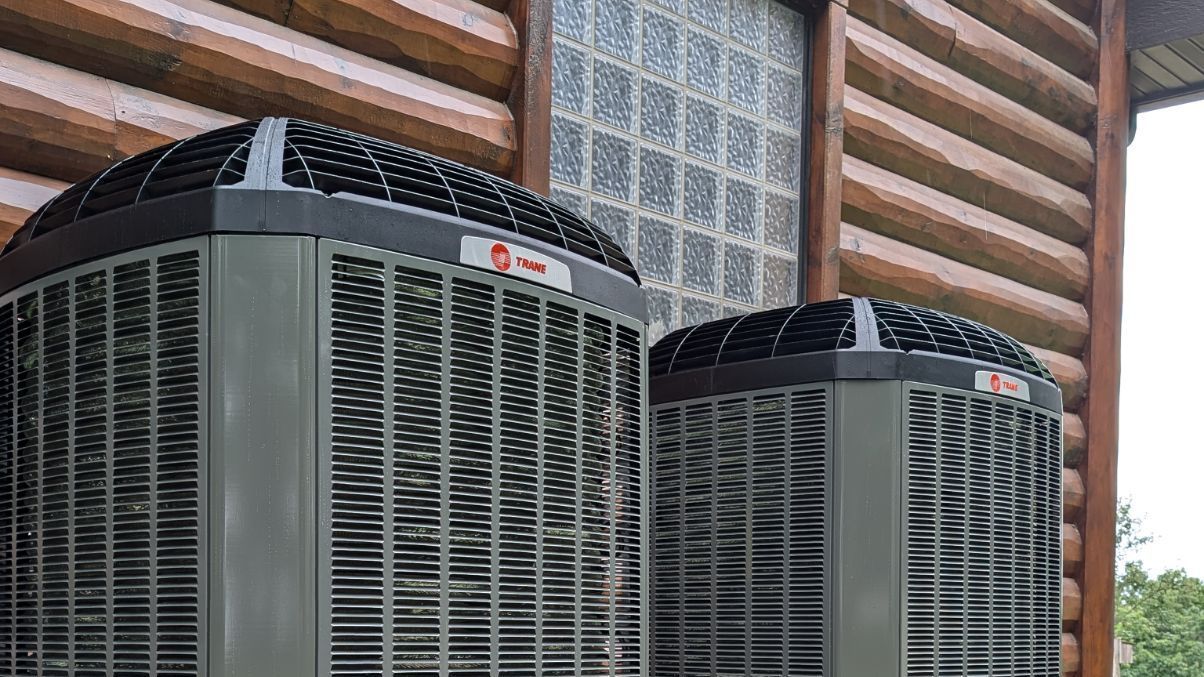 Two air conditioners are sitting next to each other on the side of a log cabin.