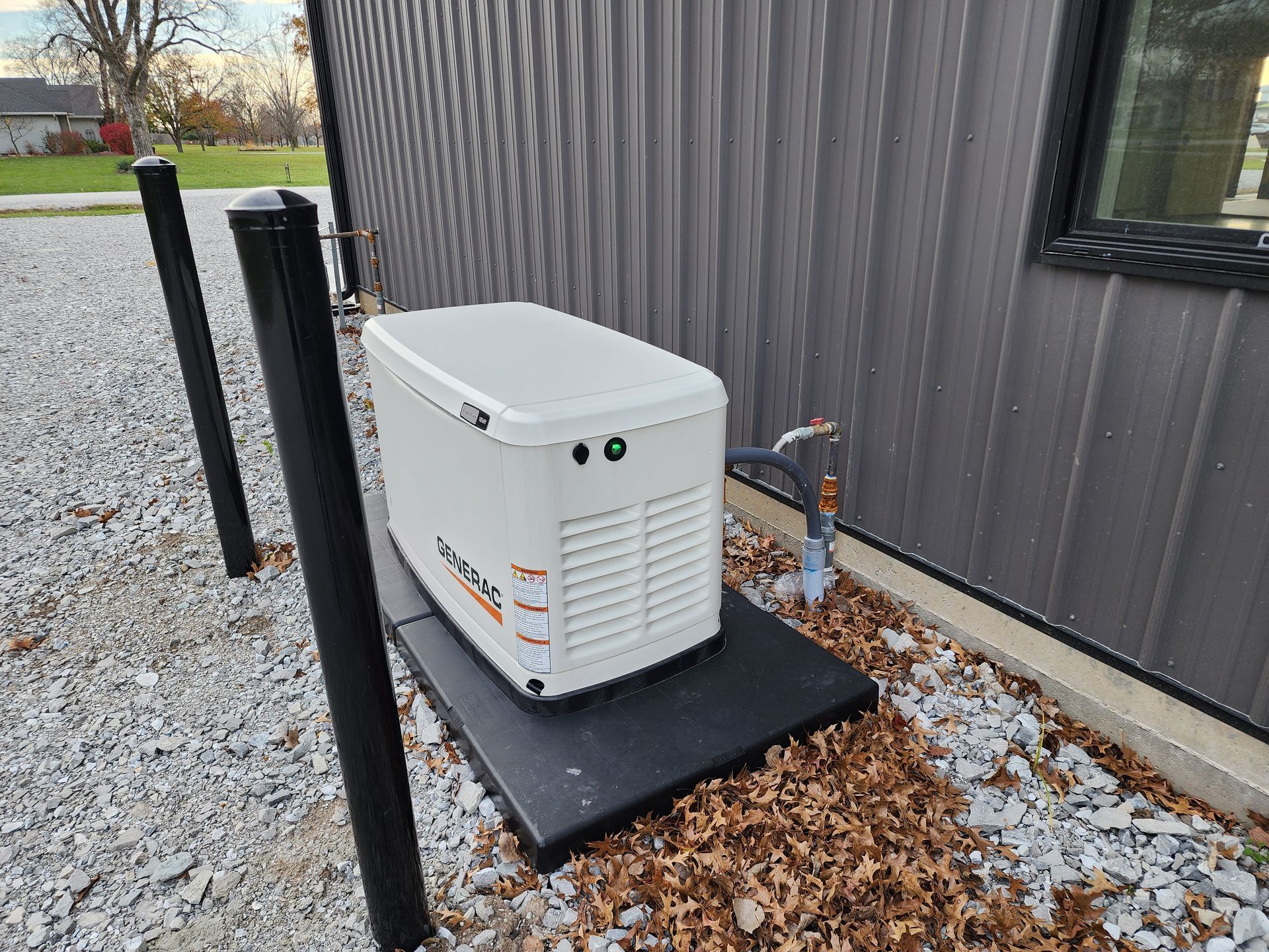 Generator unit on a black base next to a building with gray siding and gravel.