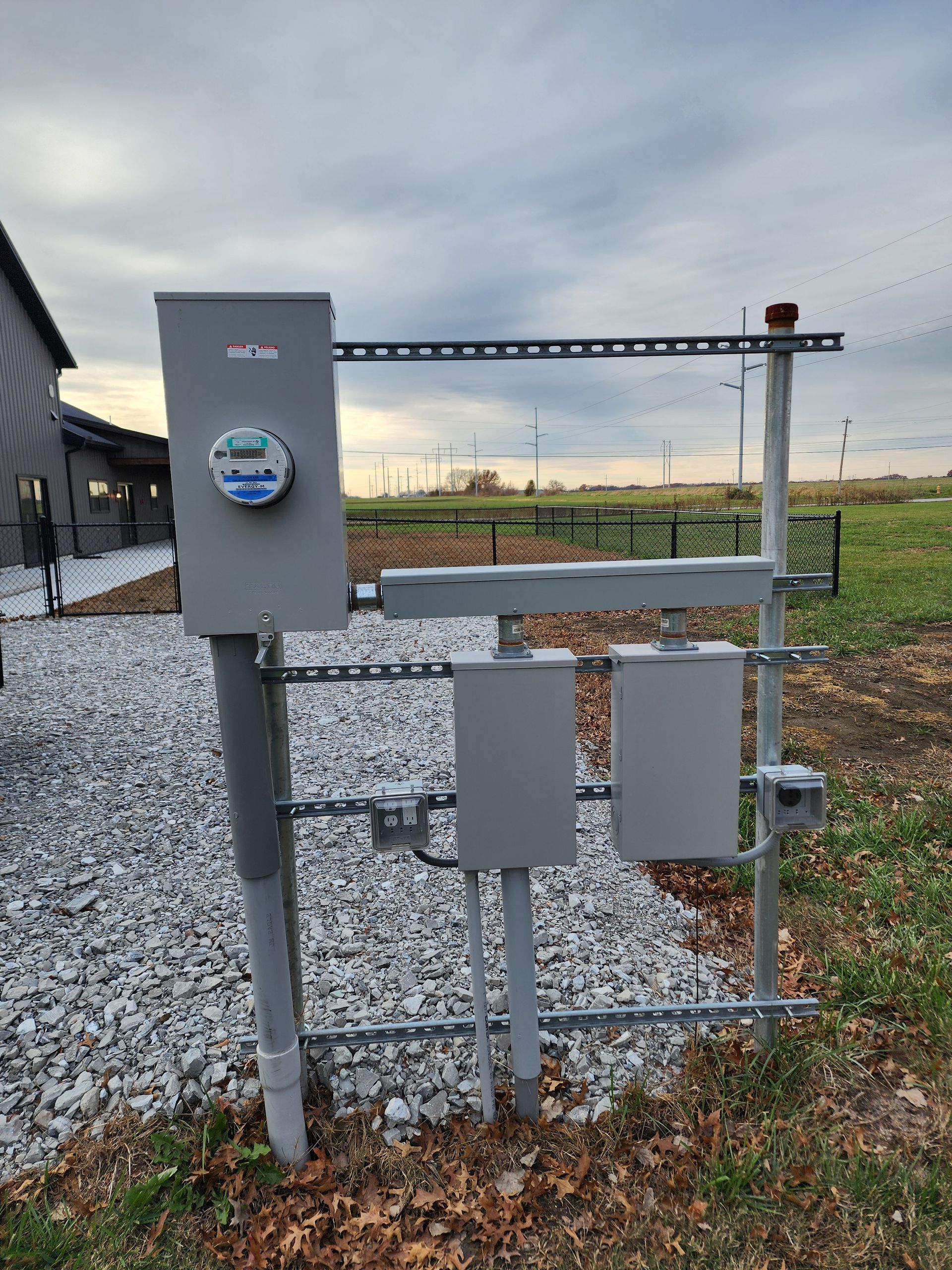 A electrical box is sitting on top of a pile of gravel next to a field.