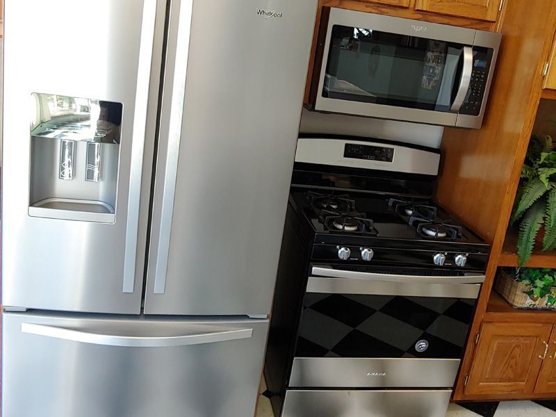 Stainless steel refrigerator, gas range, and microwave in a kitchen with wooden cabinets.