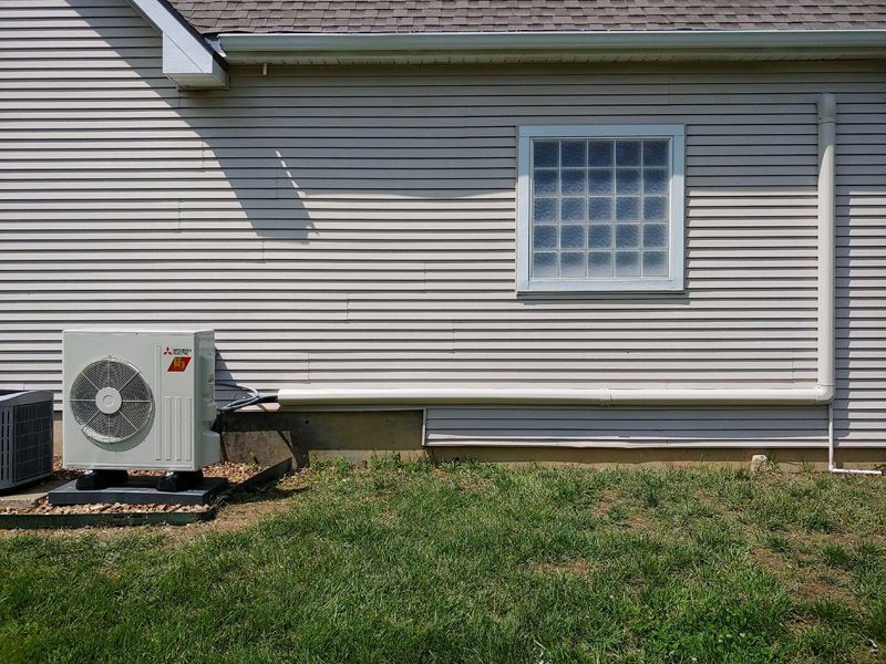 Exterior of a house with AC unit, white siding, a window, and a grassy yard.