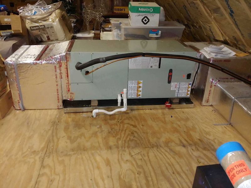 HVAC unit in an attic with ductwork, insulation, and various storage items.