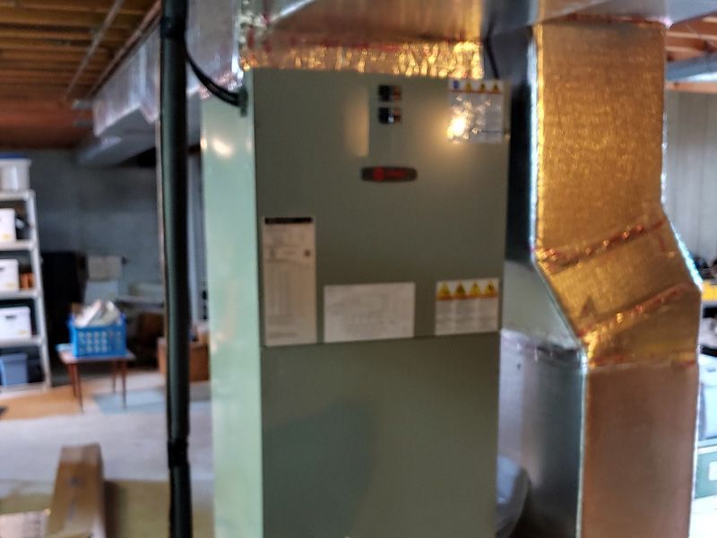 Furnace in basement with ductwork. Light green metal unit with labels, metallic ductwork.