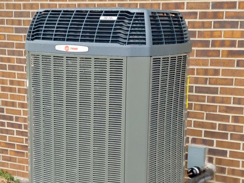 Gray Trane air conditioner unit against a brick wall.