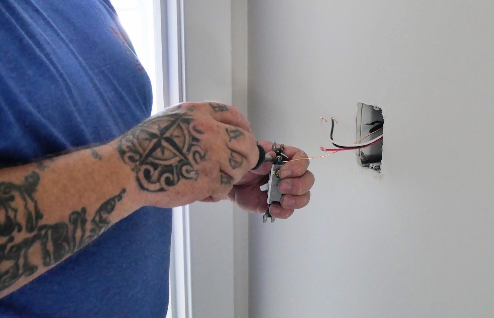 A person with a tattoo on their arm is working on a light switch.
