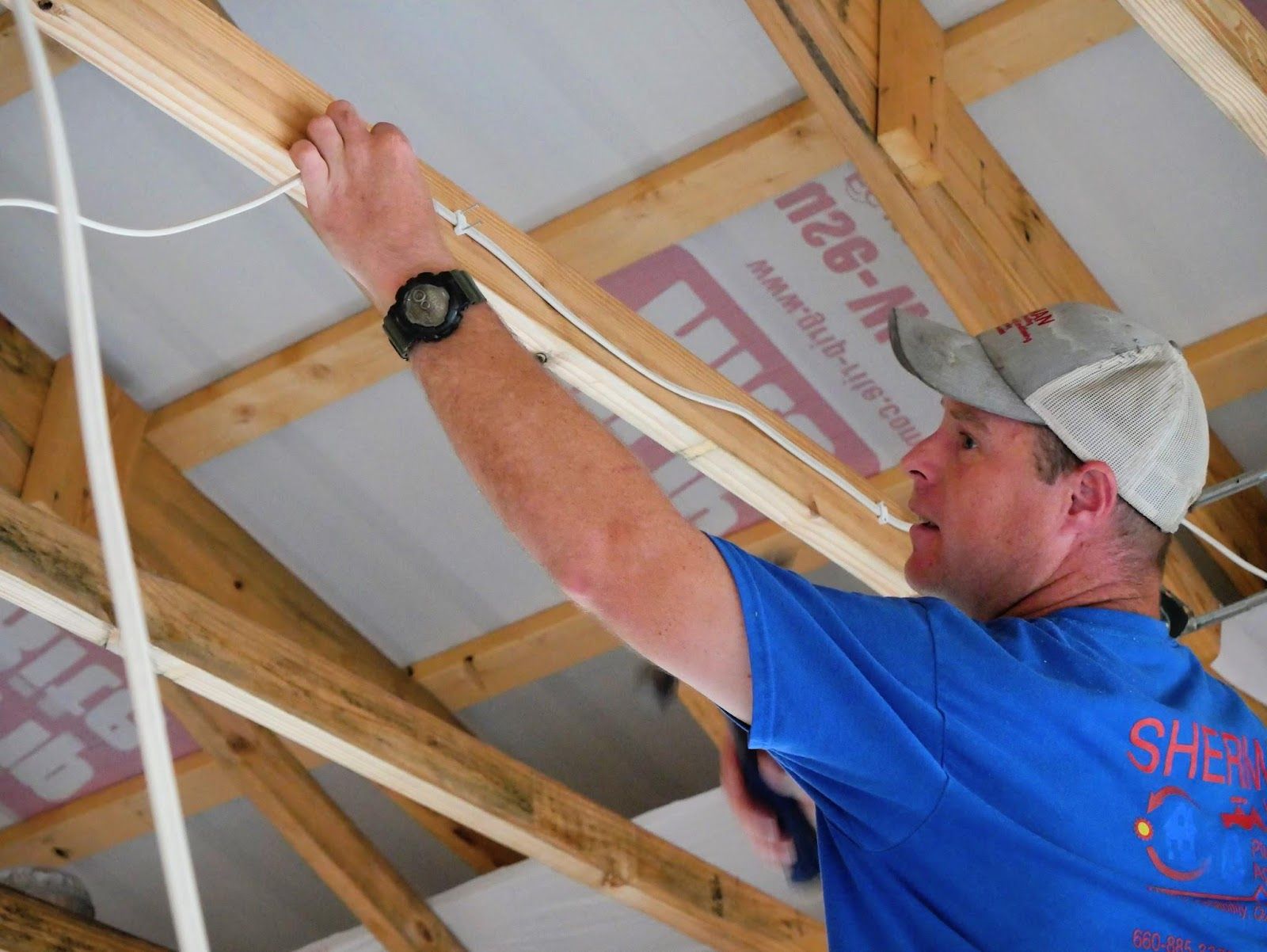 A man in a blue shirt is working on the ceiling of a building.