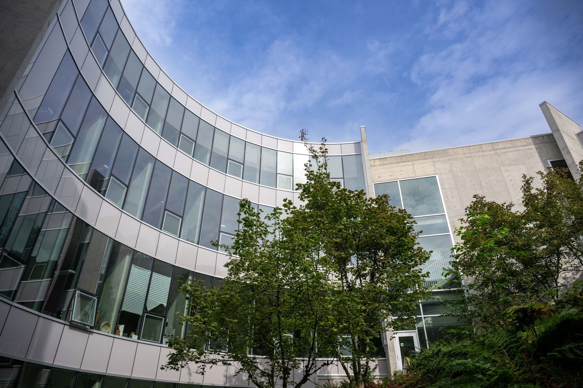Curved glass office building with trees in front under a blue sky