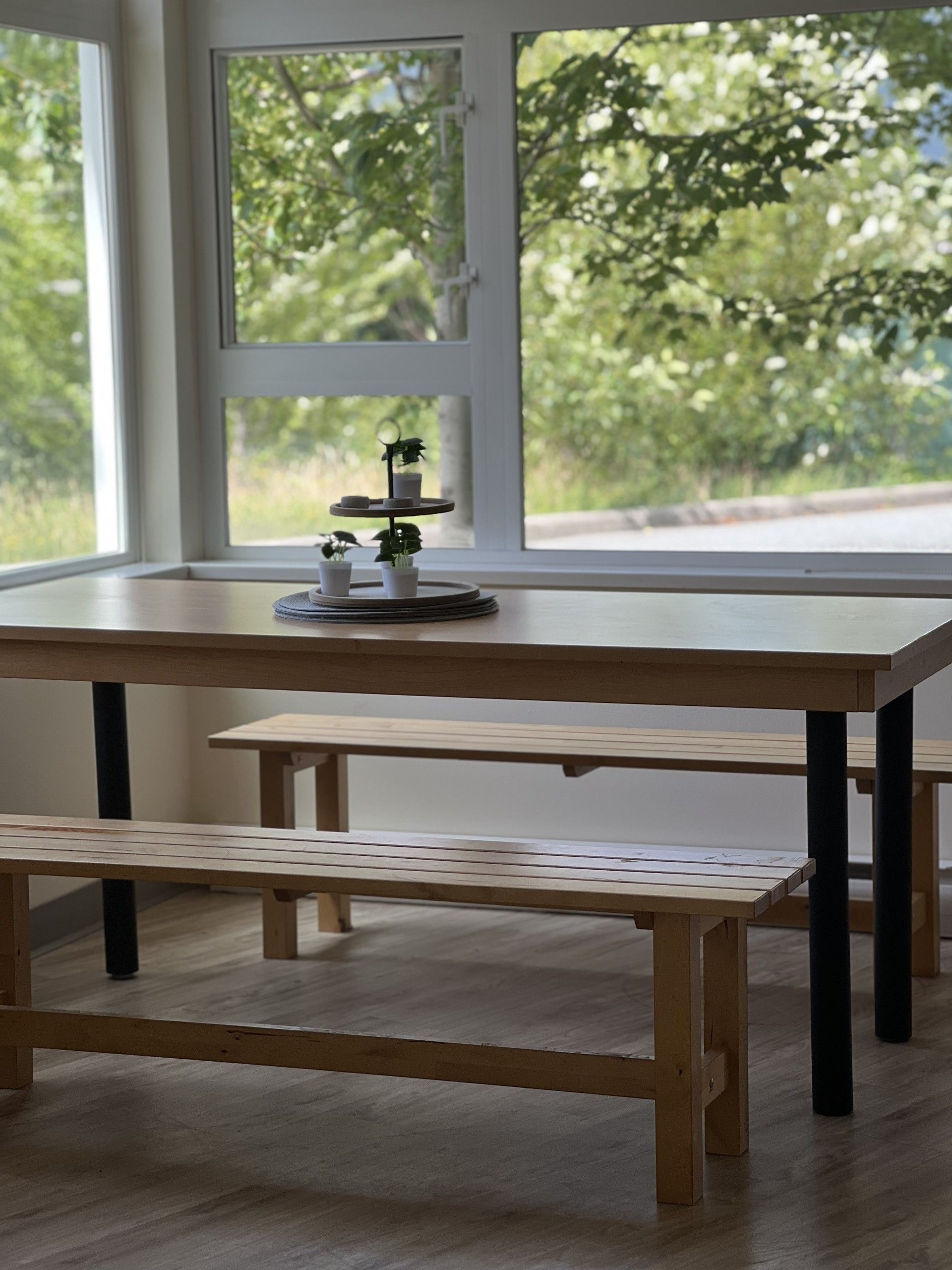 Wooden table and benches by a window, with greenery outside. Small plants on the table.