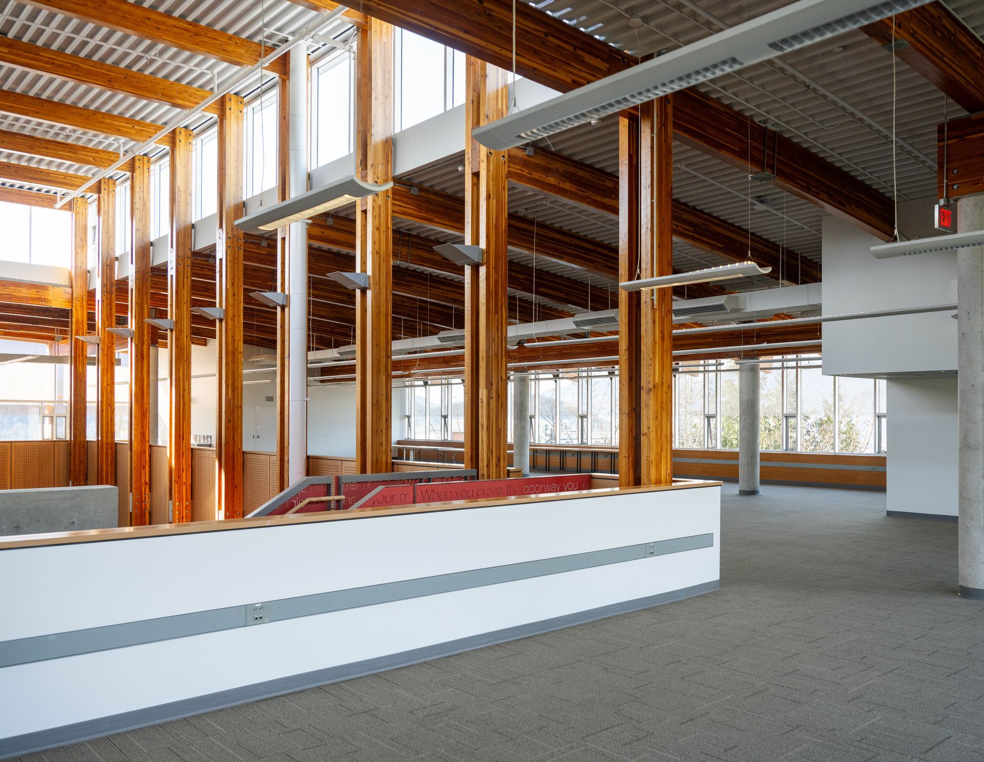 Modern open office interior with exposed wooden beams, white walls, and gray carpet.