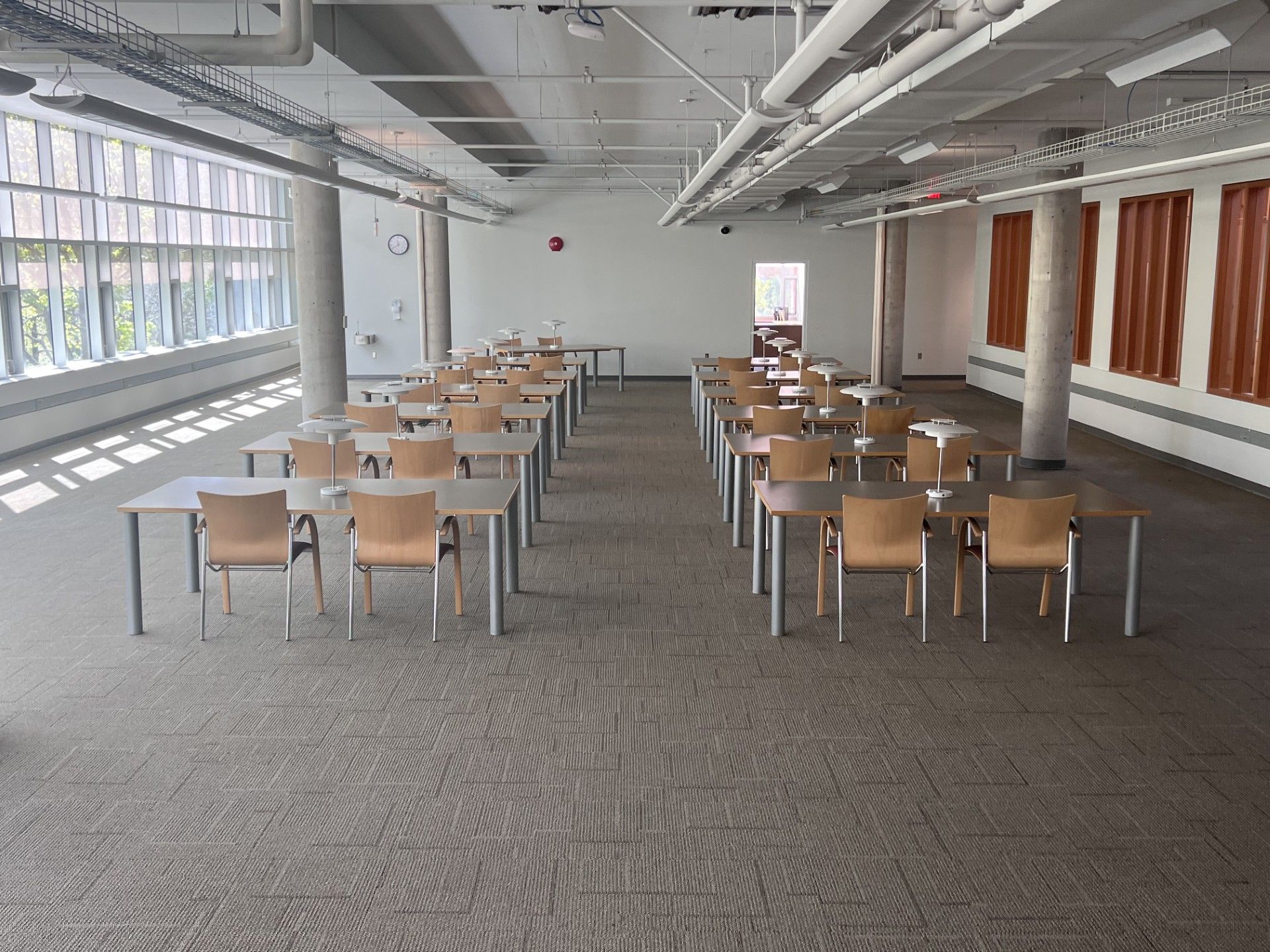 Empty modern meeting room with rows of wooden chairs, tables, and large windows along the left wall