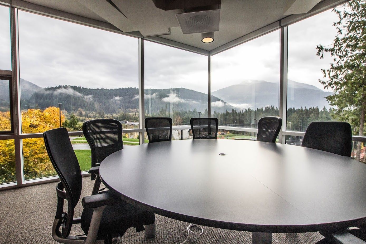 Round outdoor table with black chairs under a covered patio, overlooking a misty hillside view