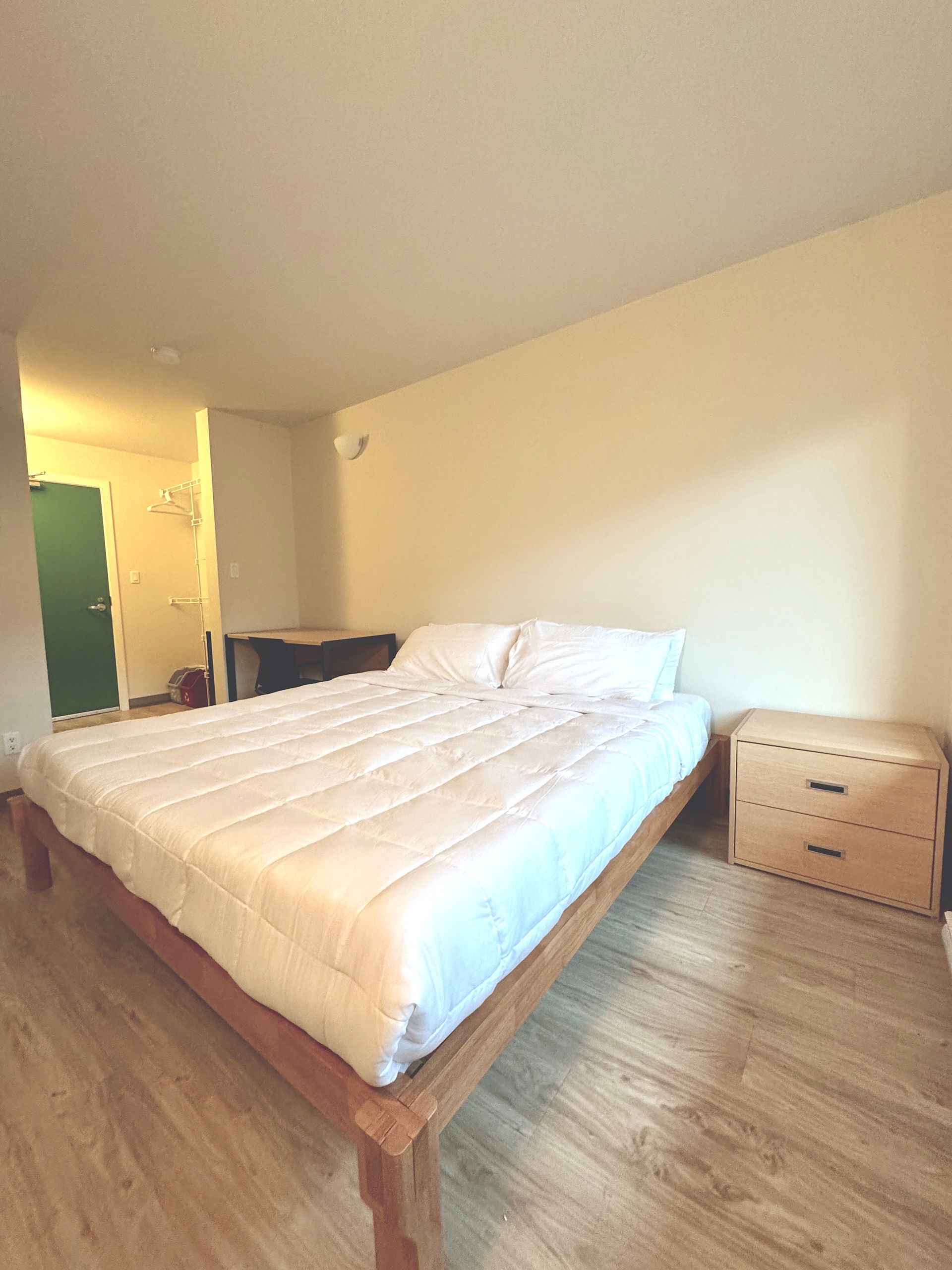 Bright bedroom with a large bed, wooden nightstand, and open doorway to a lit bathroom.