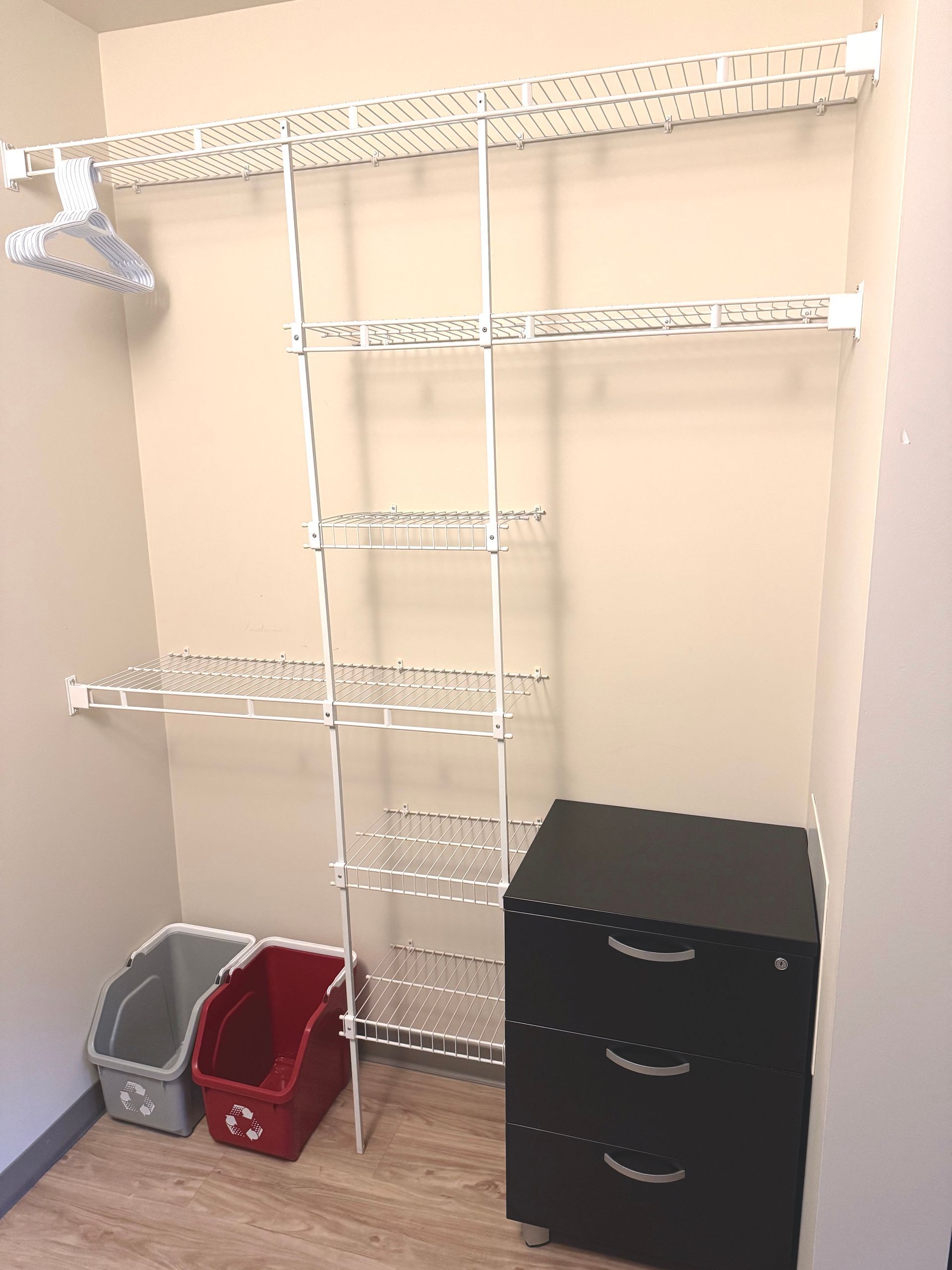 Empty closet with white wire shelving, black drawers, and red and gray bins on the floor.
