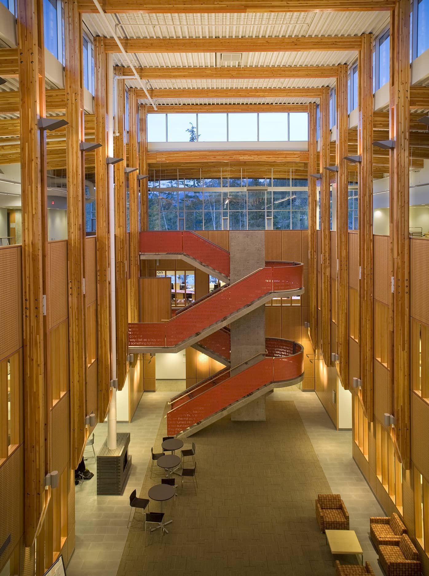 Modern atrium with tall wooden beams, red staircases, and seating in a bright interior