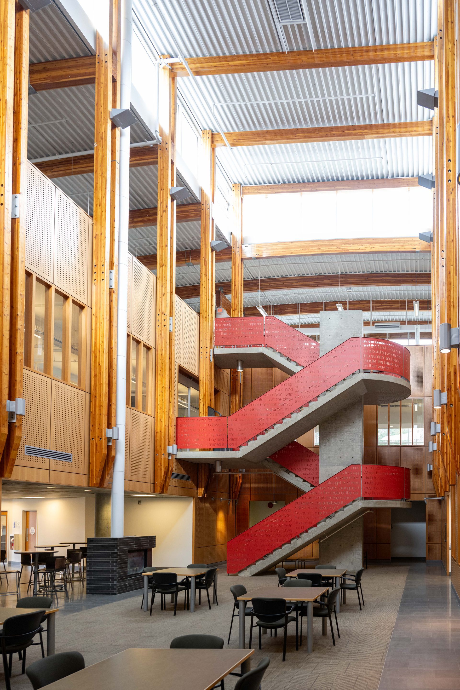 Atrium with red staircases, tall wooden beams, and café tables under a glass roof