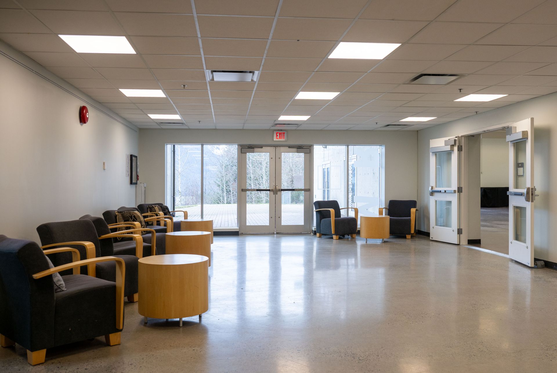 Empty waiting room with black chairs, round tables, and large windows by the entrance.