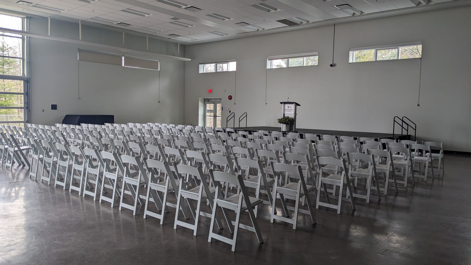 Rows of white folding chairs set up in a large empty indoor hall.