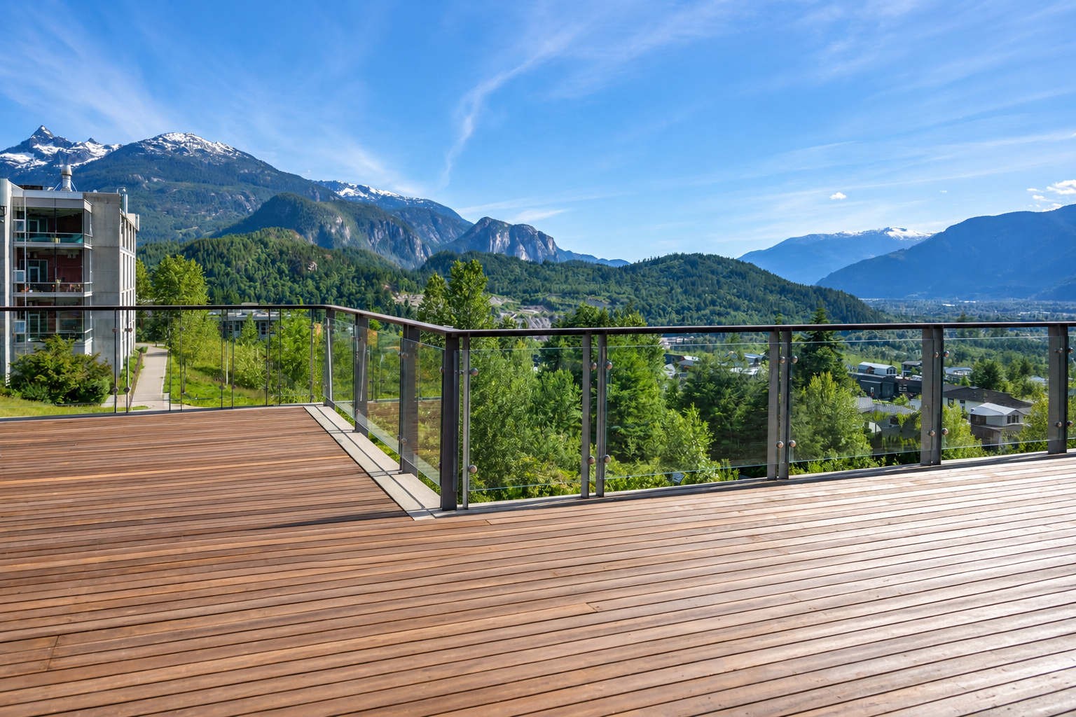 Wooden deck with glass railing overlooking green mountains under a clear blue sky