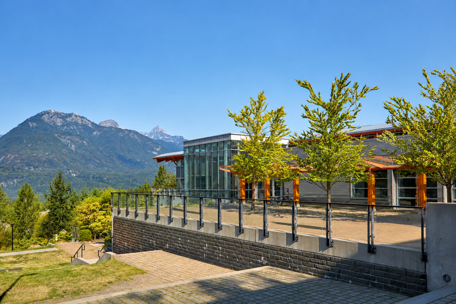 Modern glass building with stone terrace and mountains under a clear blue sky