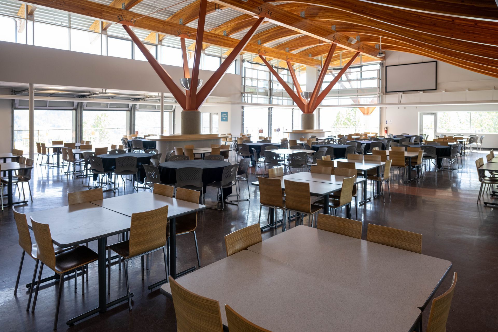 Spacious modern cafeteria with tables, chairs, and large windows under wooden ceiling beams