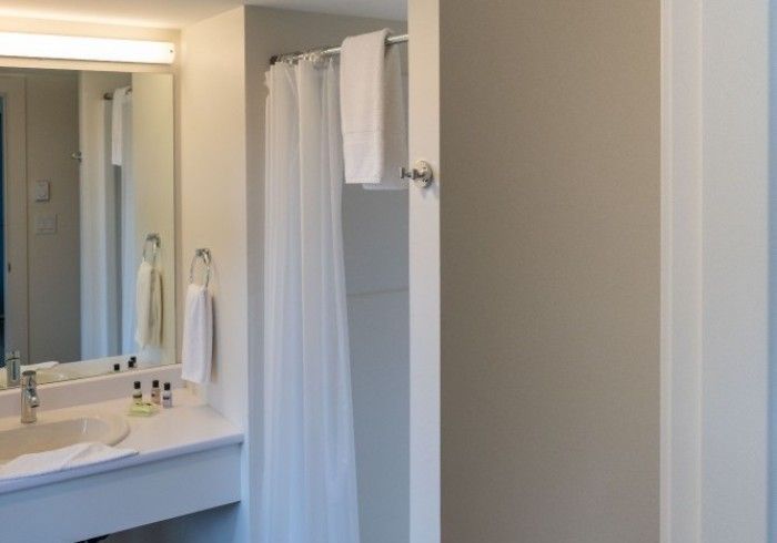 Bathroom with a white vanity and sink, large mirror, and shower stall with curtain. Towels are hanging.