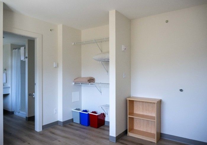 Empty closet with shelving, a small bookshelf, and recycling bins; doorway to a bathroom on the left.