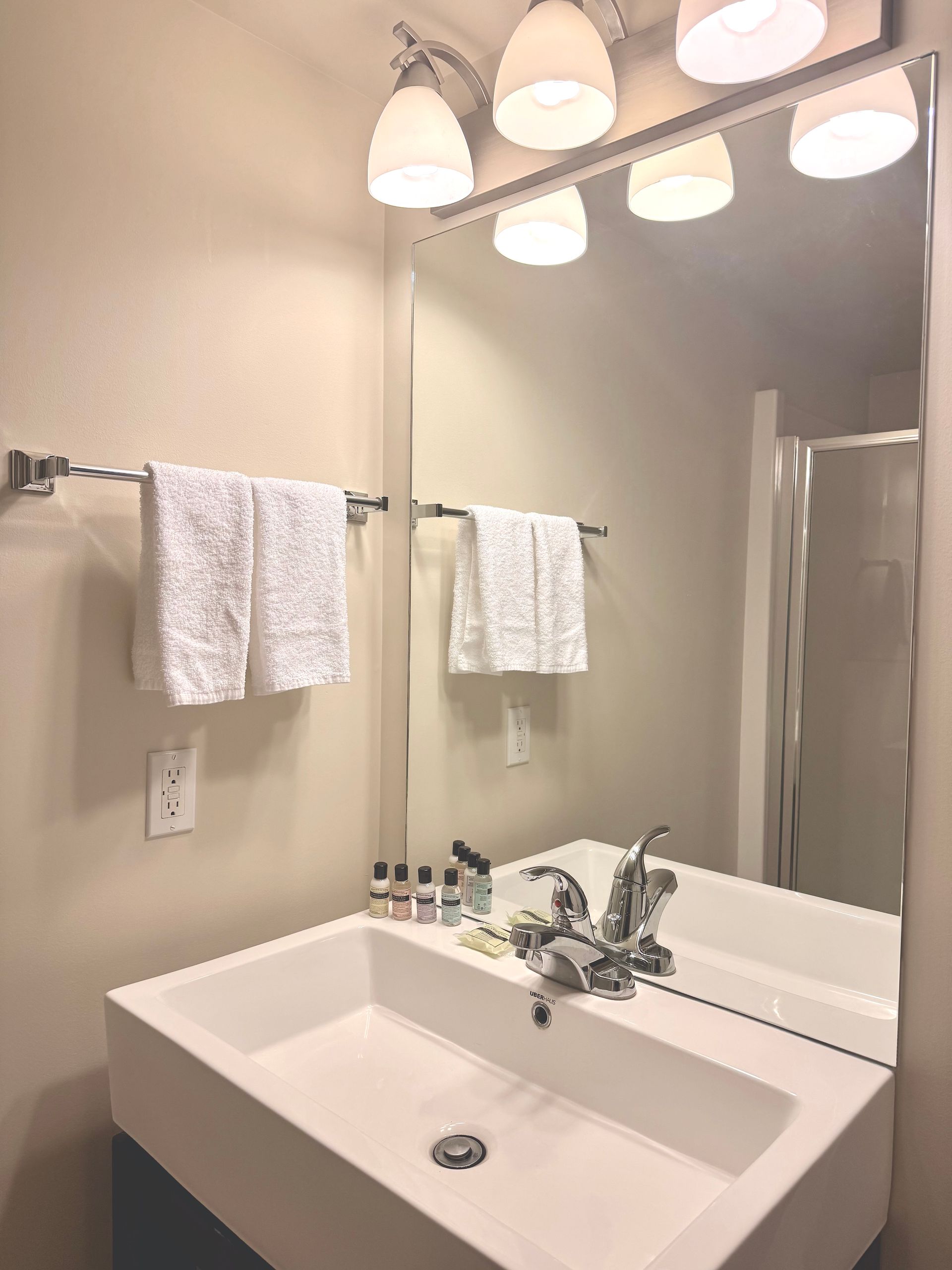 Bathroom sink and mirror with vanity lights, white towels, and toiletries on the counter.