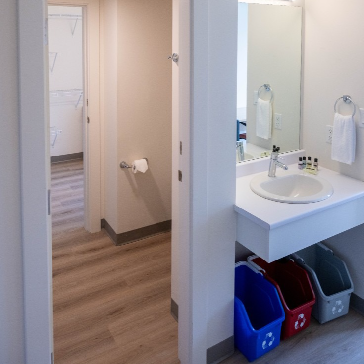 Bathroom with sink, mirror, and recycling bins; hallway with closet visible.