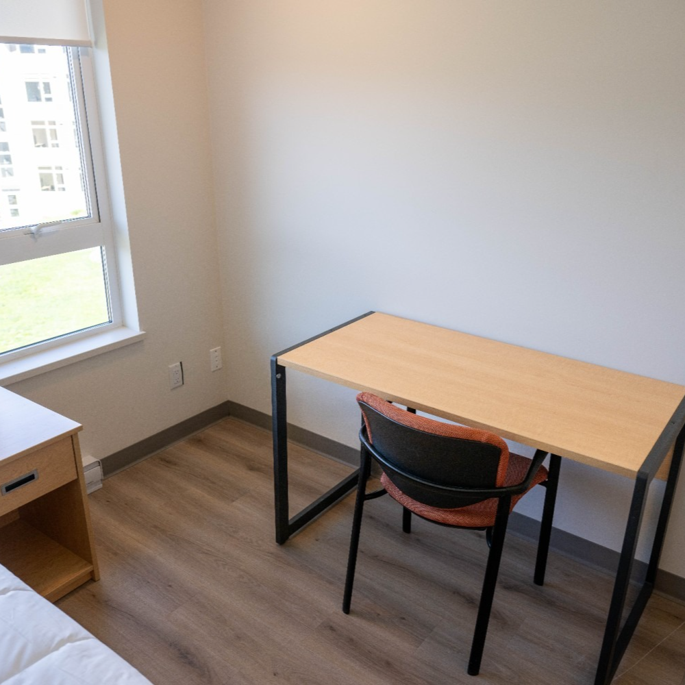 Empty room with a desk and chair by a window. Light wood floor and walls.