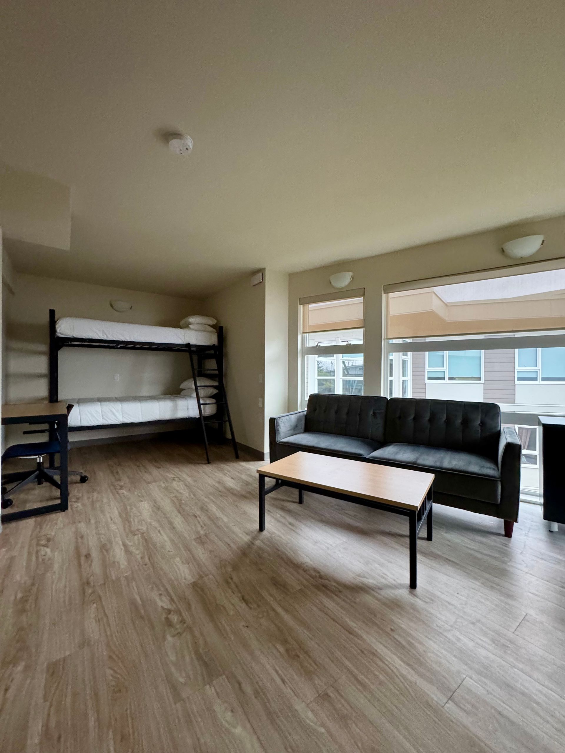 Bright living room with bunk bed, black sofa, coffee table, and large windows with blinds