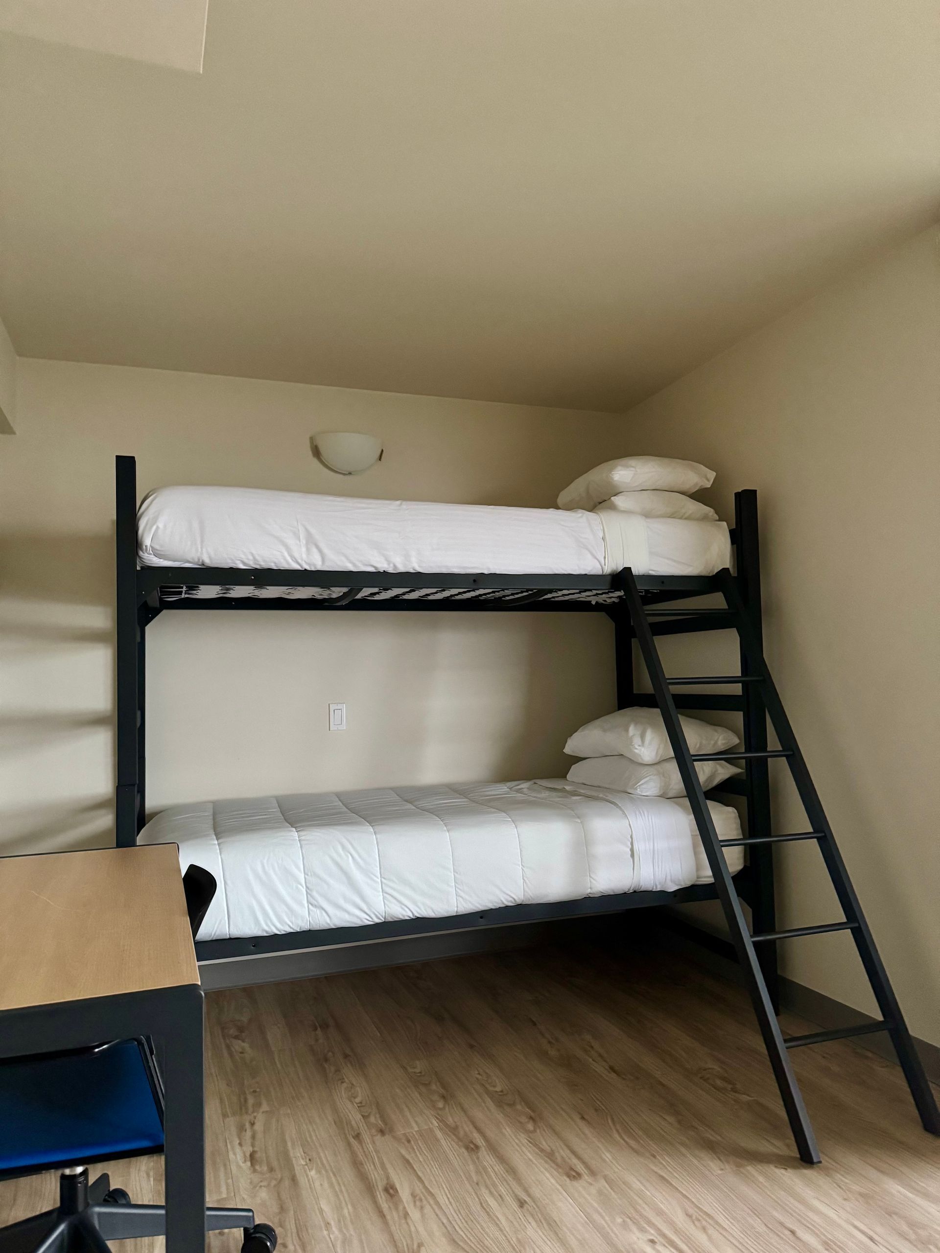 Black metal bunk bed with white bedding and ladder in a small room with wood flooring