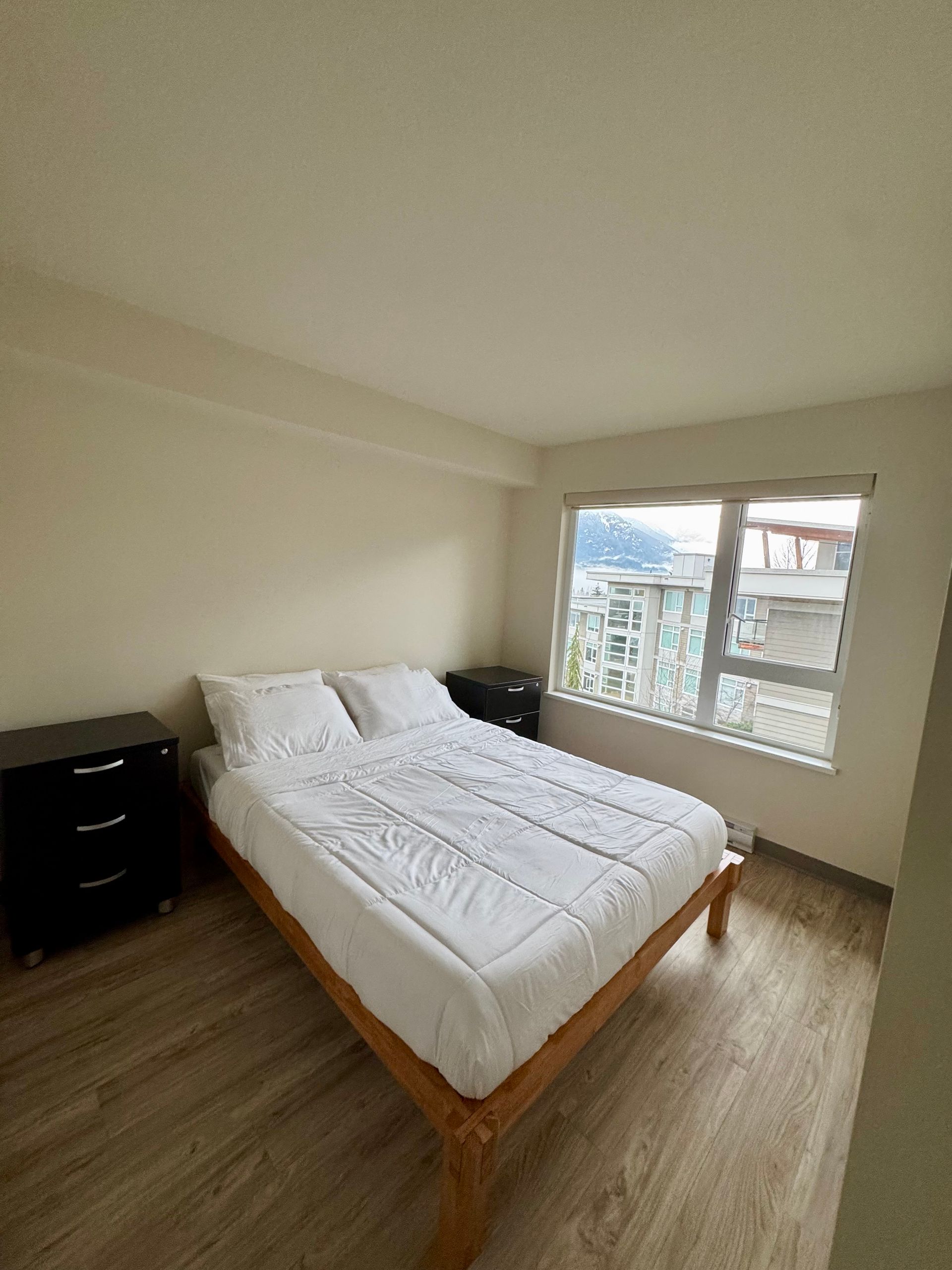 Small bedroom with a double bed, two nightstands, and large windows overlooking a balcony.