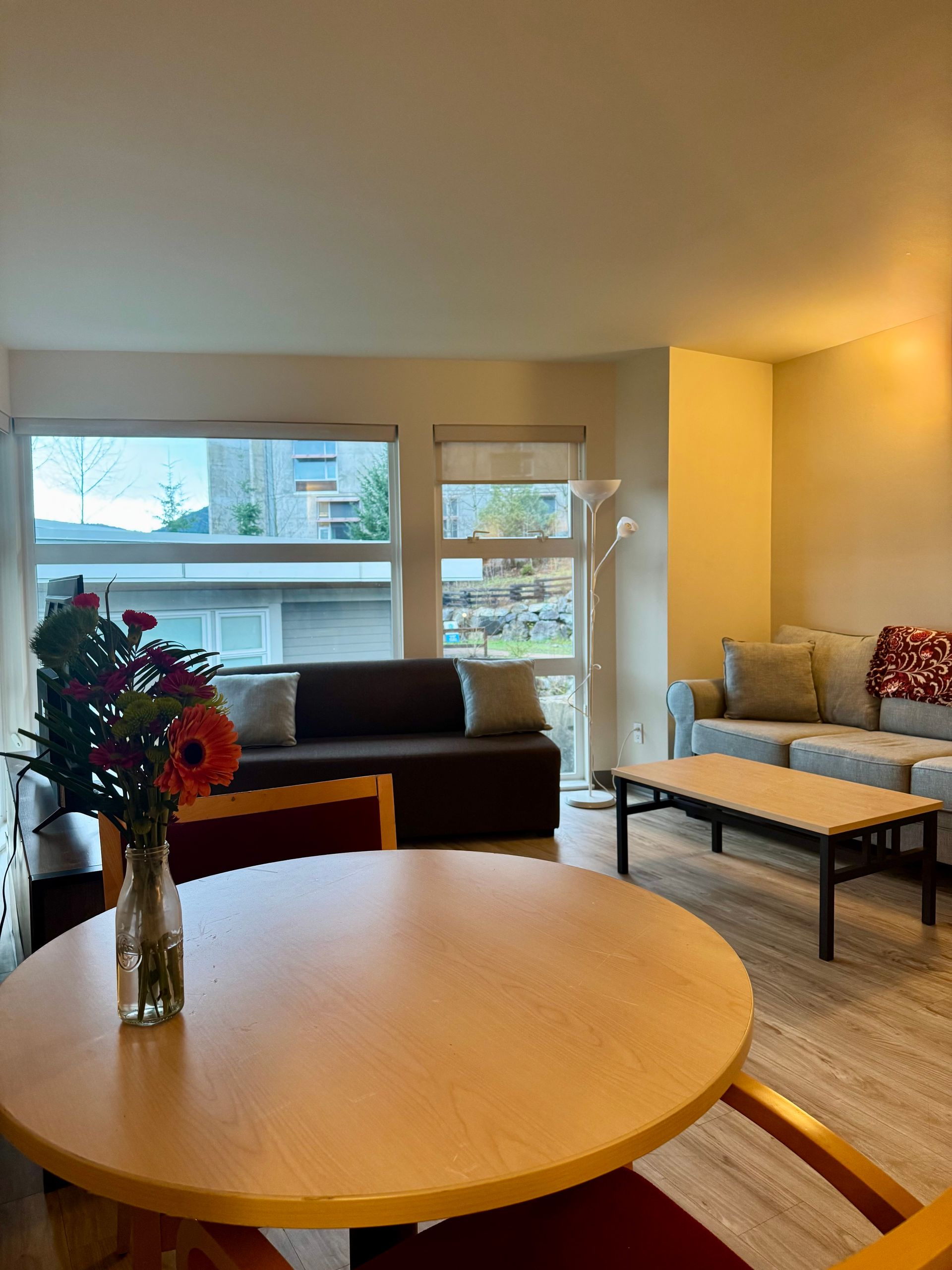 Bright living room with round wooden table, sofa, bench, and large windows overlooking city views