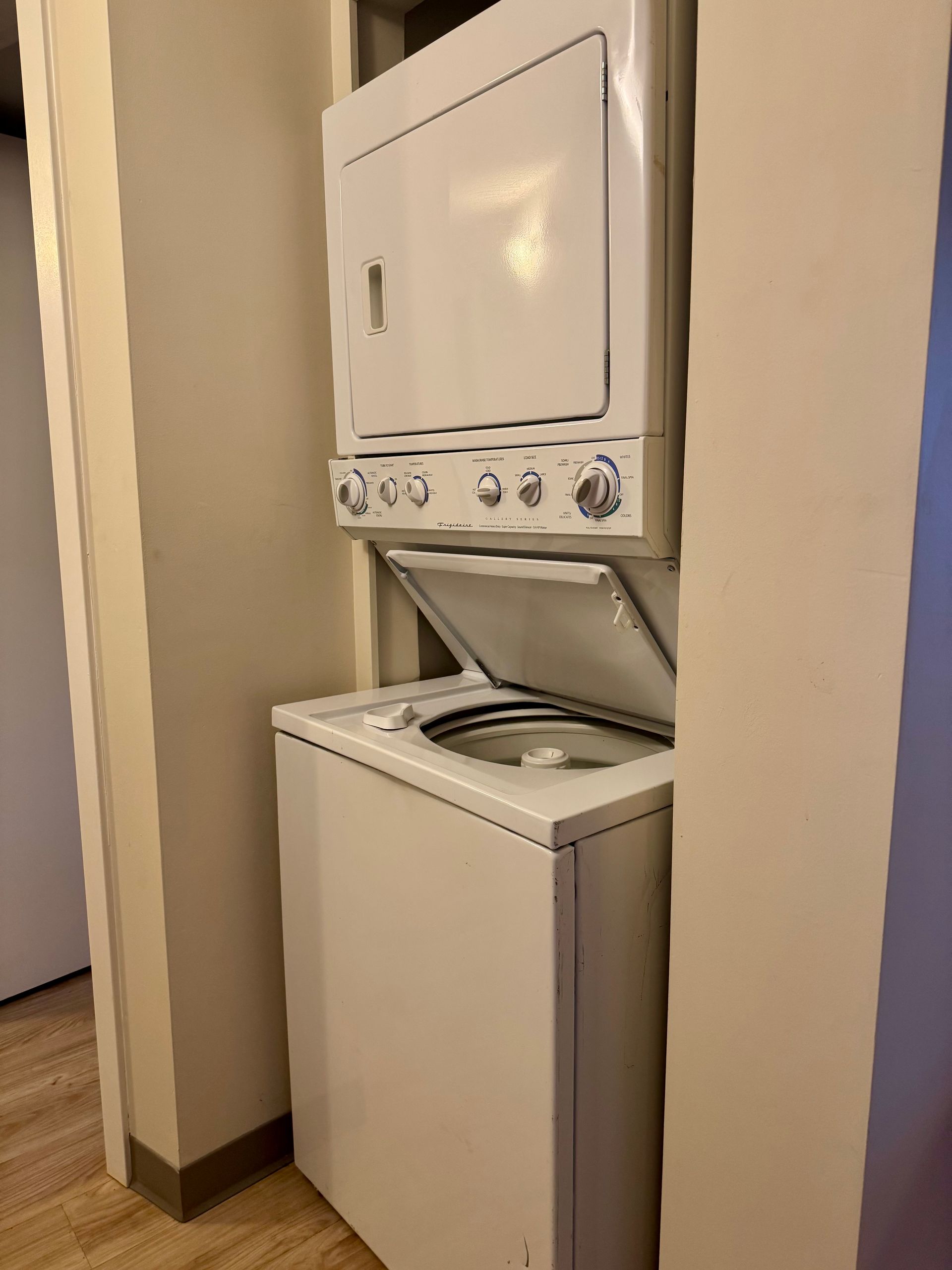 Stacked white washer and dryer in a narrow hallway, front-loading washer open beneath the dryer.