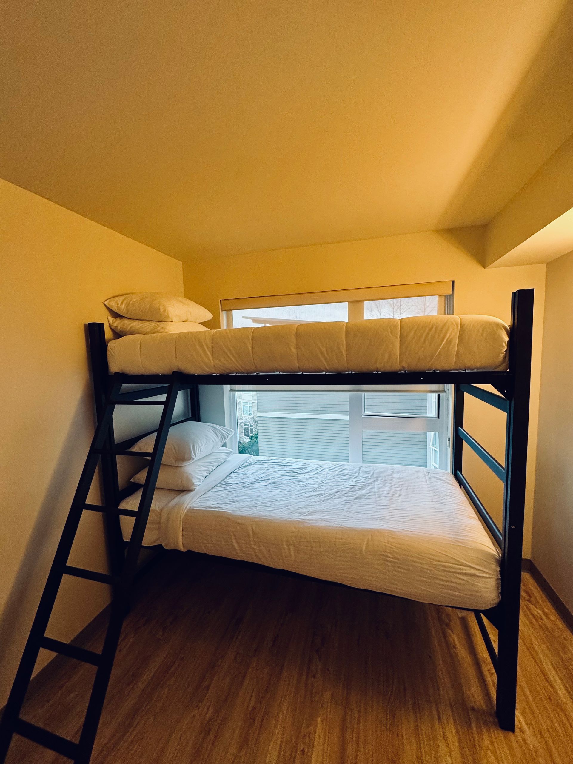 Black metal bunk bed in a small attic room with white bedding and wooden floor