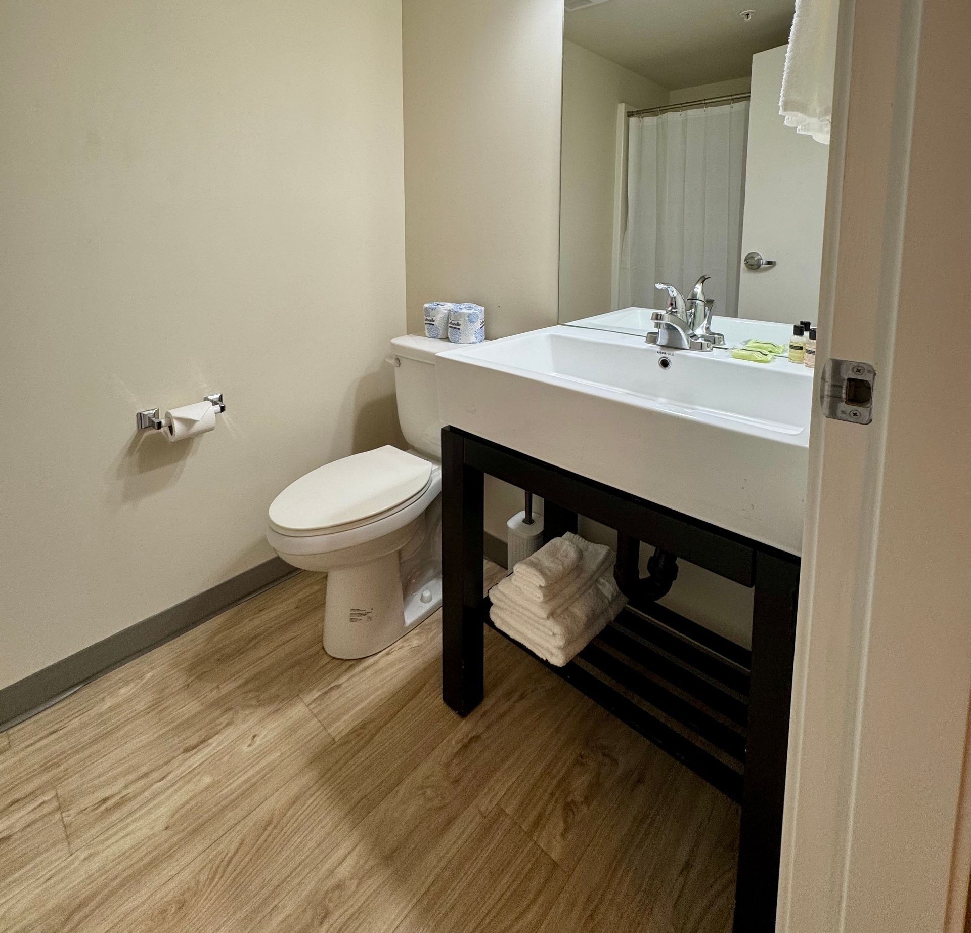 Modern bathroom with white vanity, toilet, beige walls, and wood-look floor
