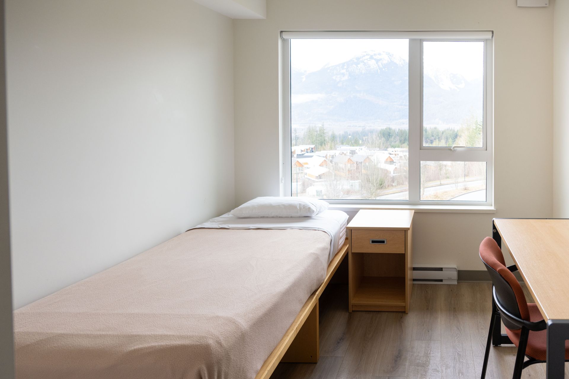 Bedroom with a single bed, nightstand, desk, and a large window with a mountain view.