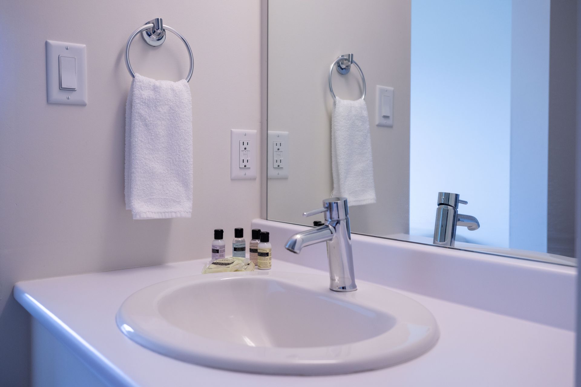 Bathroom sink with mirror, chrome faucet, white counter, and hand towel on a wall hook.