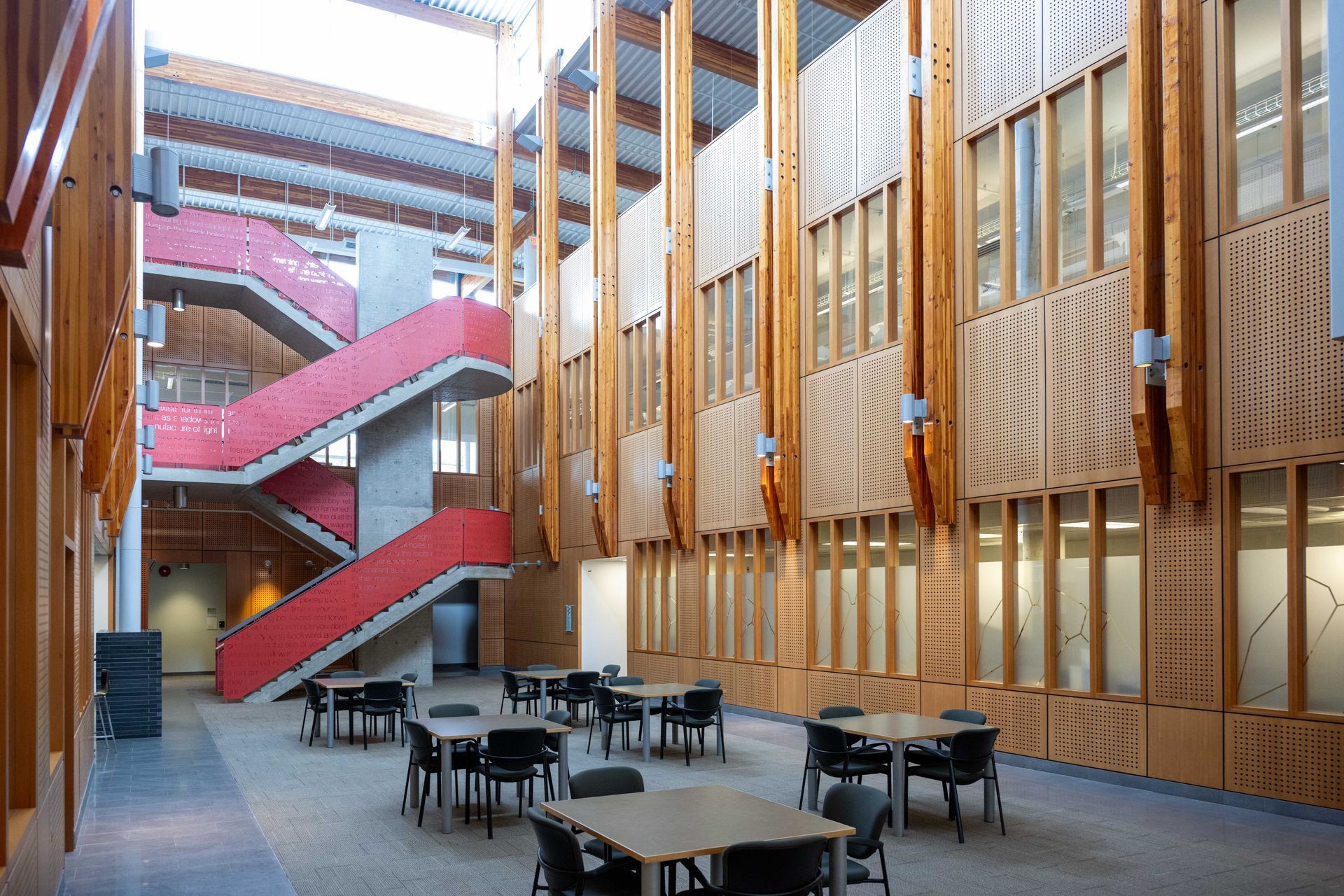 Interior of a building with red stairs, wooden columns, and tables with chairs.
