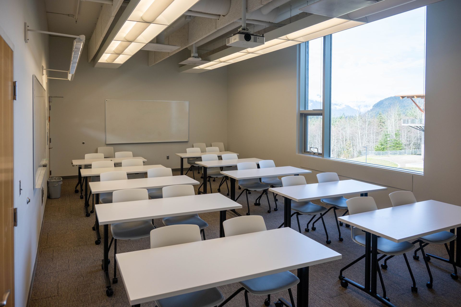 Empty classroom with rows of desks, whiteboard, and large windows overlooking mountains.