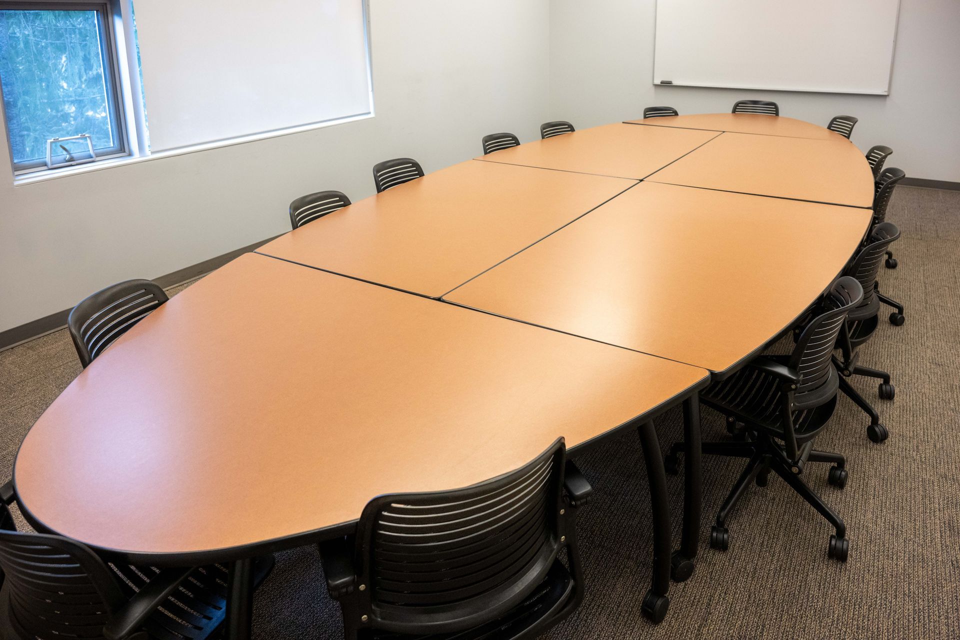 Empty conference room with a long oval table, black chairs, and a whiteboard on the wall