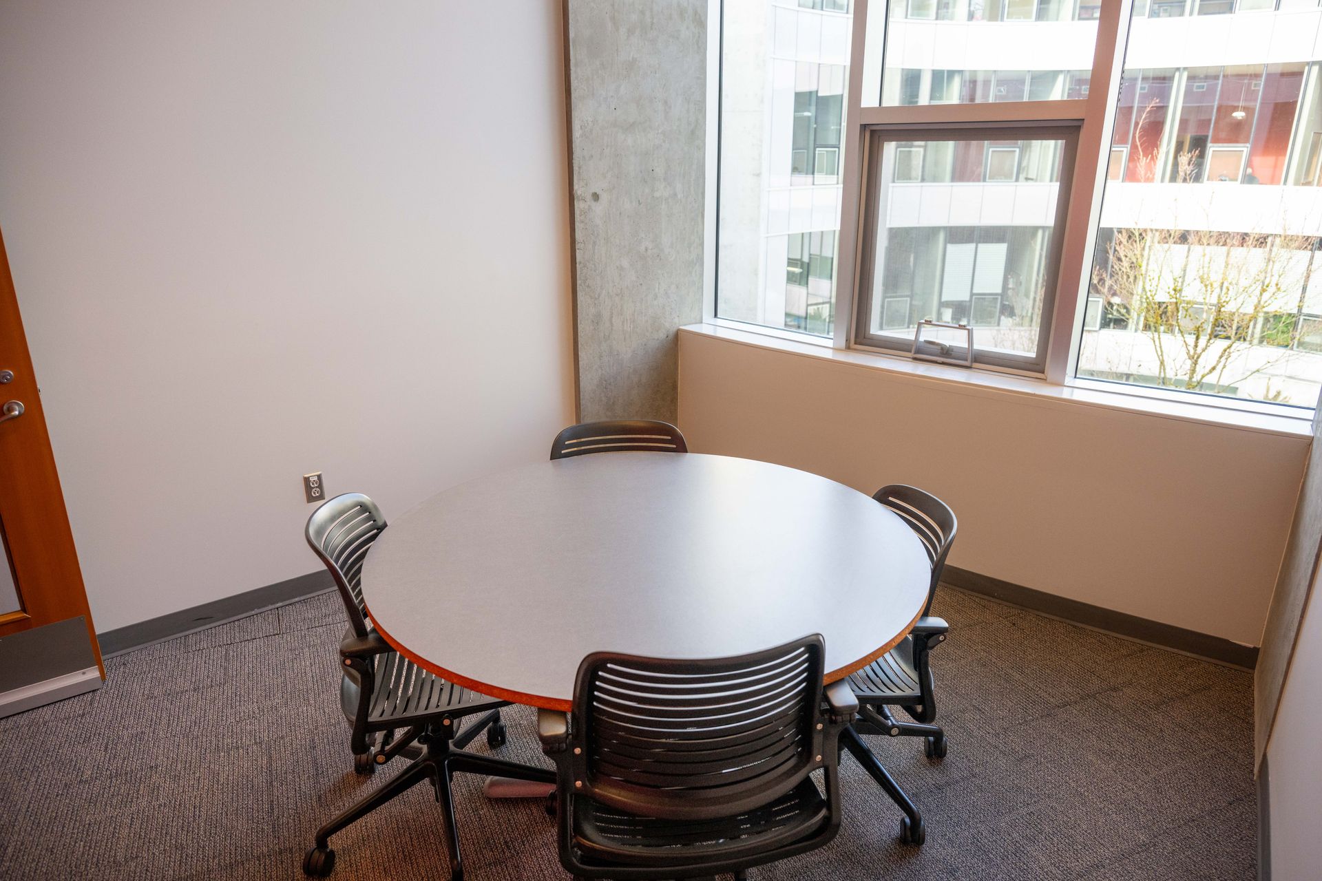 Small conference room with a round table and four chairs beside large windows.