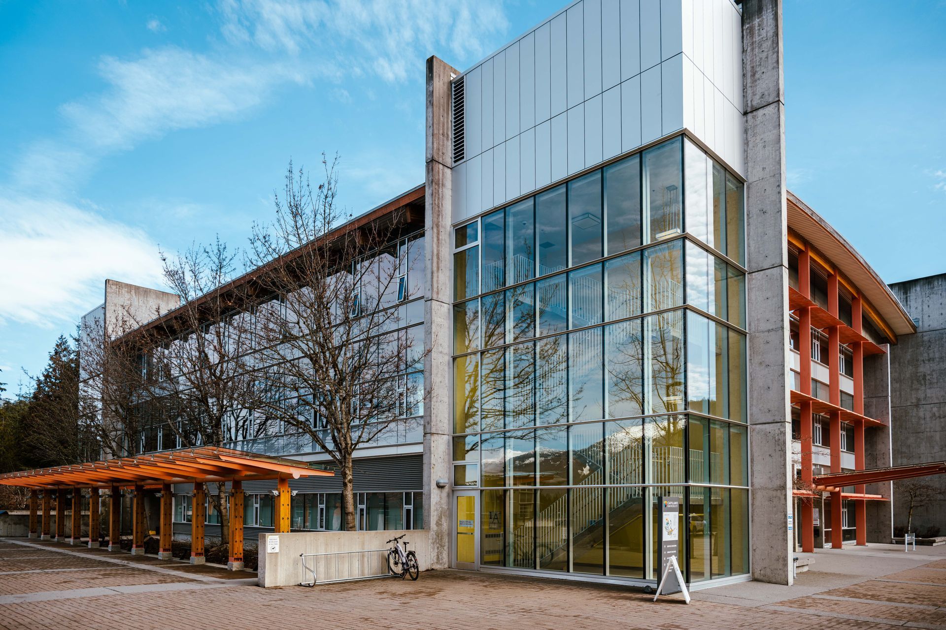 Modern building with glass front, concrete and wood accents, under a blue sky.